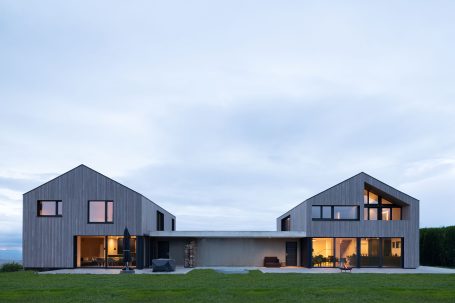 Zwei moderne, asymmetrische Häuser mit großen Fenstern in ländlicher Umgebung.